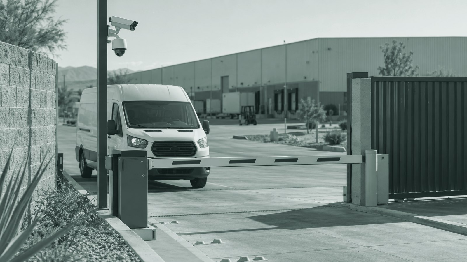 Camioneta de reparto esperando frente a la pluma de la entrada de vehículos, con cámaras de seguridad en el poste